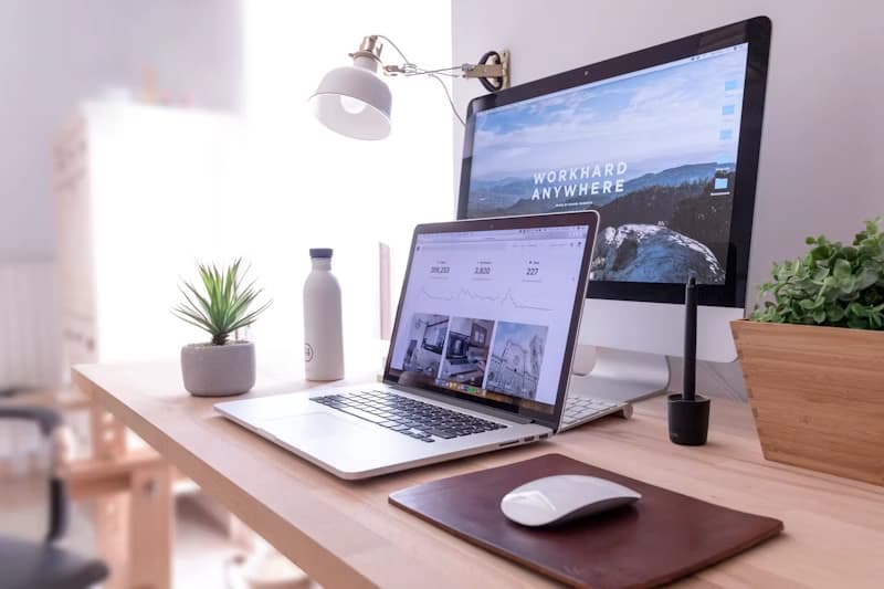 A laptop and computer on a bright wooden desk that is used for writing alt text on images.